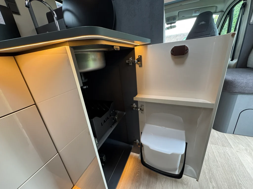 Interiér karavanu Laika, část kuchyně s dřezem a skříňkou na odpadky. Moderní design a funkční uspořádání.