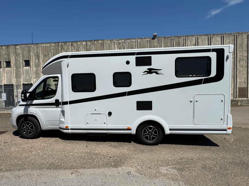 Na obrázku je karavan bílého odstínu s černými detaily. Viditelná jsou okna a boční výbava.