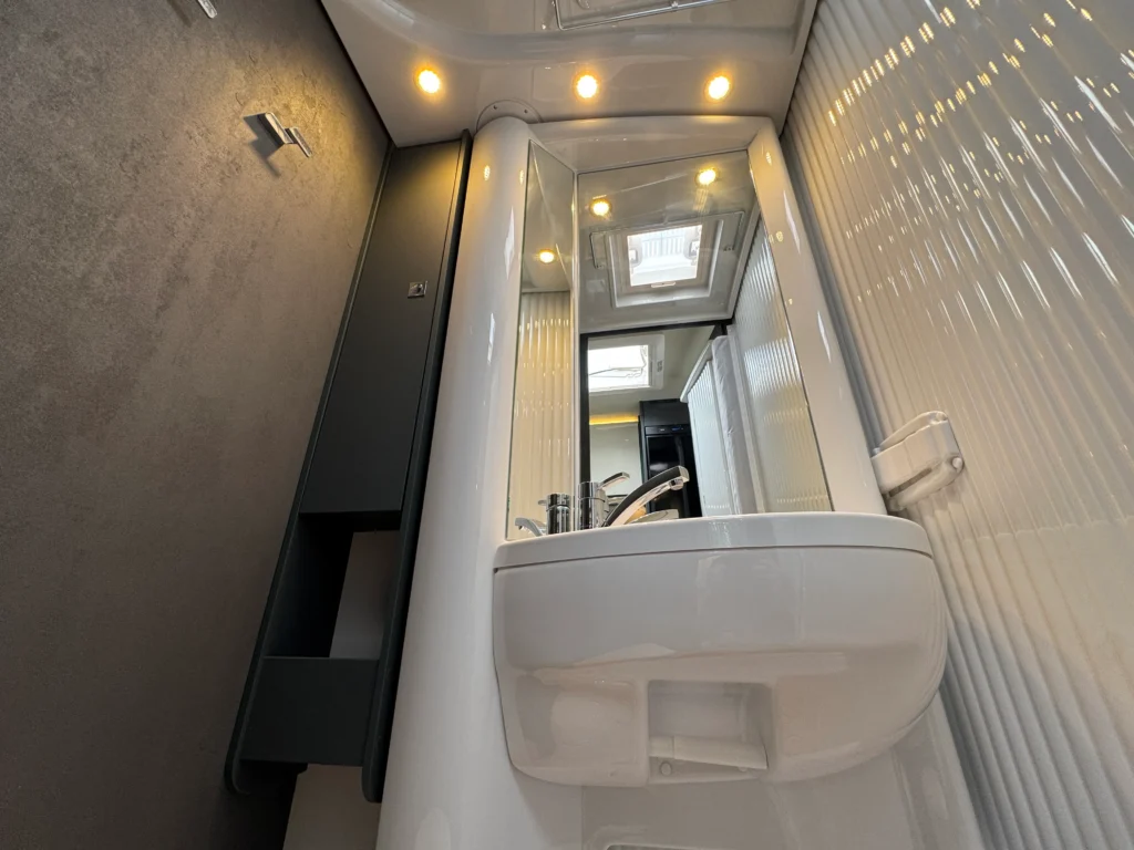 Obrázek interiéru koupelny obytného vozu, moderní design s umyvadlem a zrcadlem. Ideální pro pohodlné cestování.