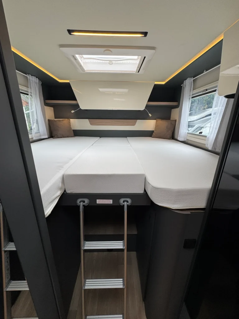 Interiér obytného přívěsu s dvojlůžkem a schůdkami. Moderní design s tematickým osvětlením a okny.