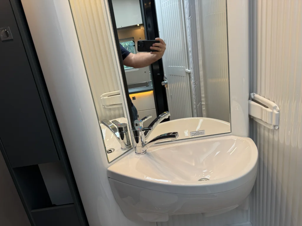 Obrázek interiéru obytného vozu s umyvadlem a zrcadlem, moderní design a praktičnost pro pohodlné cestování.