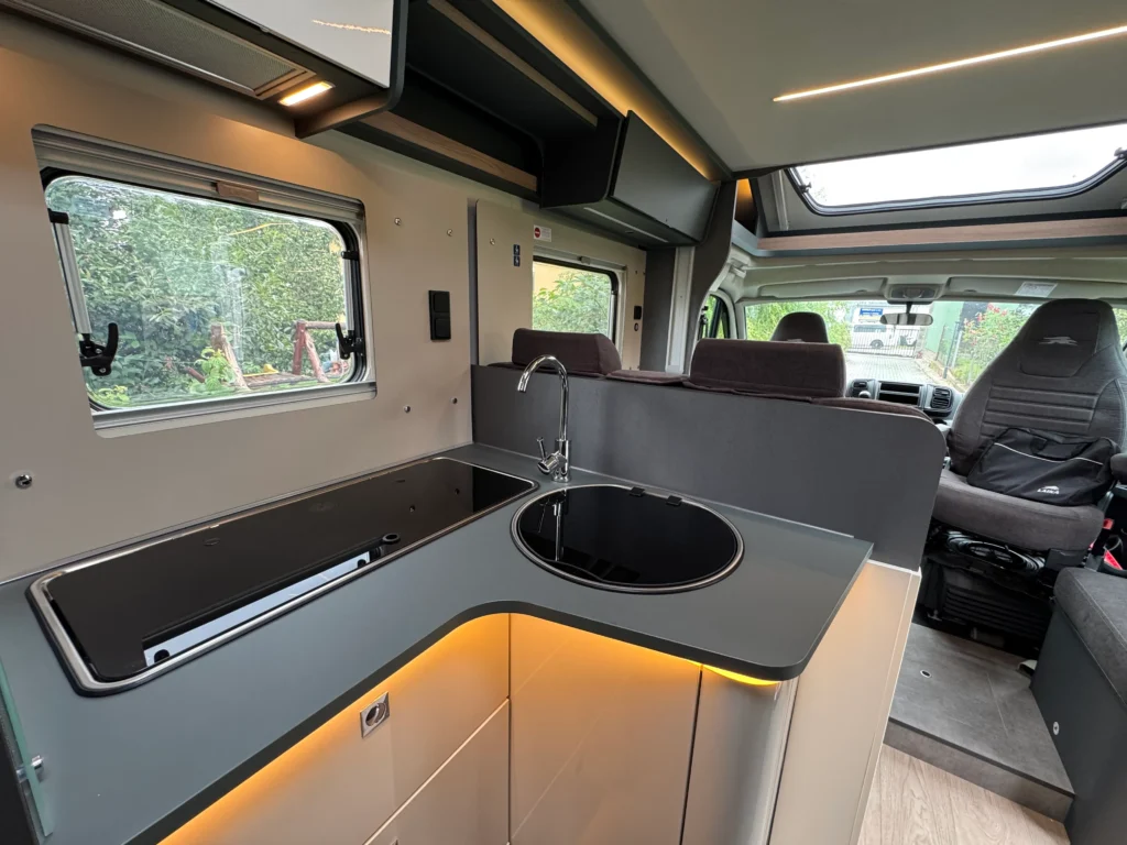 Interiér obytného auta s moderní kuchyňkou, okny a pohodlným sezením. Ideální pro cestování a kempování.