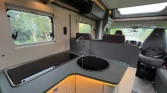 Interiér obytného auta s moderní kuchyňkou, okny a pohodlným sezením. Ideální pro cestování a kempování.