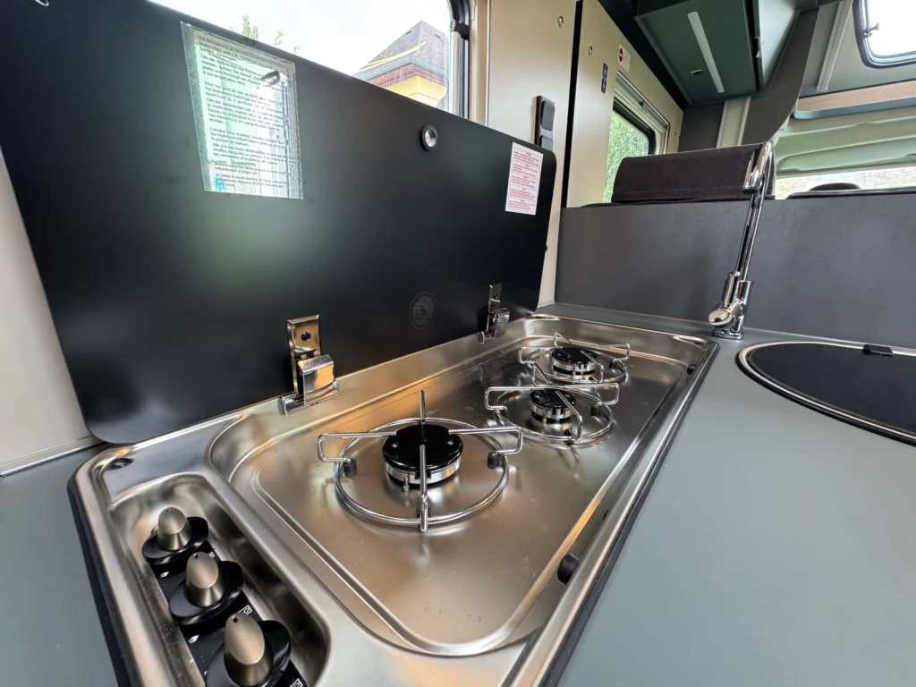 Obrázek ukazuje kuchyňku v obytném autě s moderním sporákem a dřezem. Ideální pro cestování!