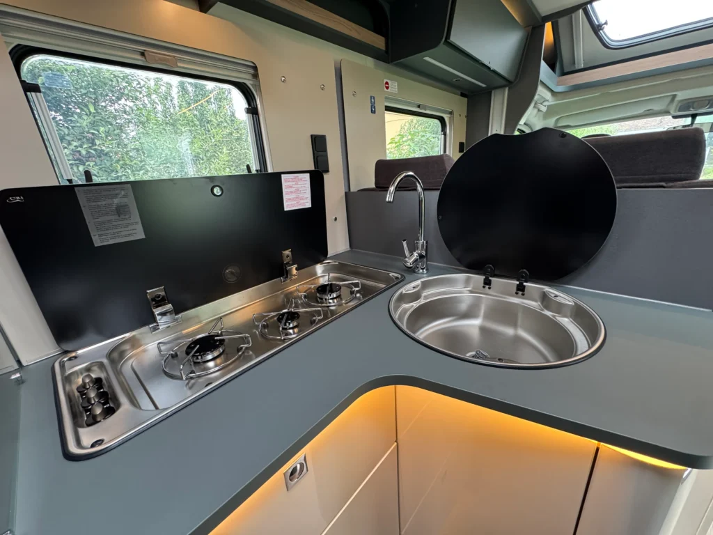 Kuchyňský kout s dřezem a vařičem v obytném voze, moderní design a funkčnost pro pohodlné vaření na cestách.