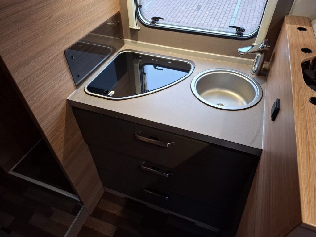 Obrázek interiéru karavanu se zabudovaným dřezem a varnou deskou. Moderní a praktické vybavení pro cestování.