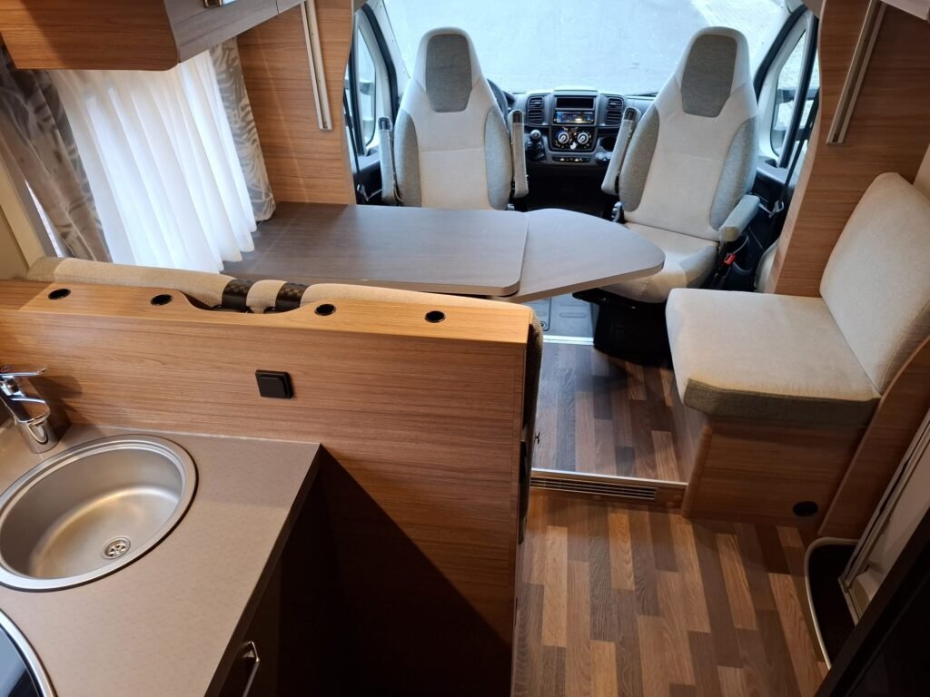 Obrázek interiéru obytného auta se světlými materiály a moderním designem. Vhodné pro pohodlné cestování.