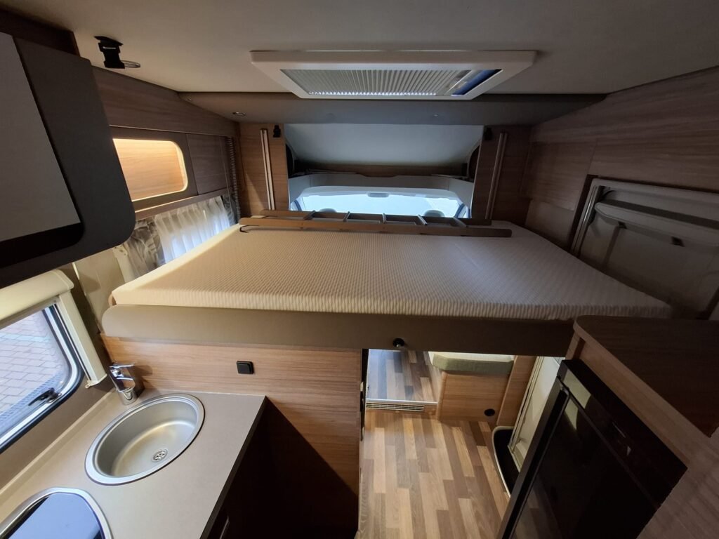 Obrázek interiéru obytného auta s komfortní kuchyňkou a rozkládací postelí.