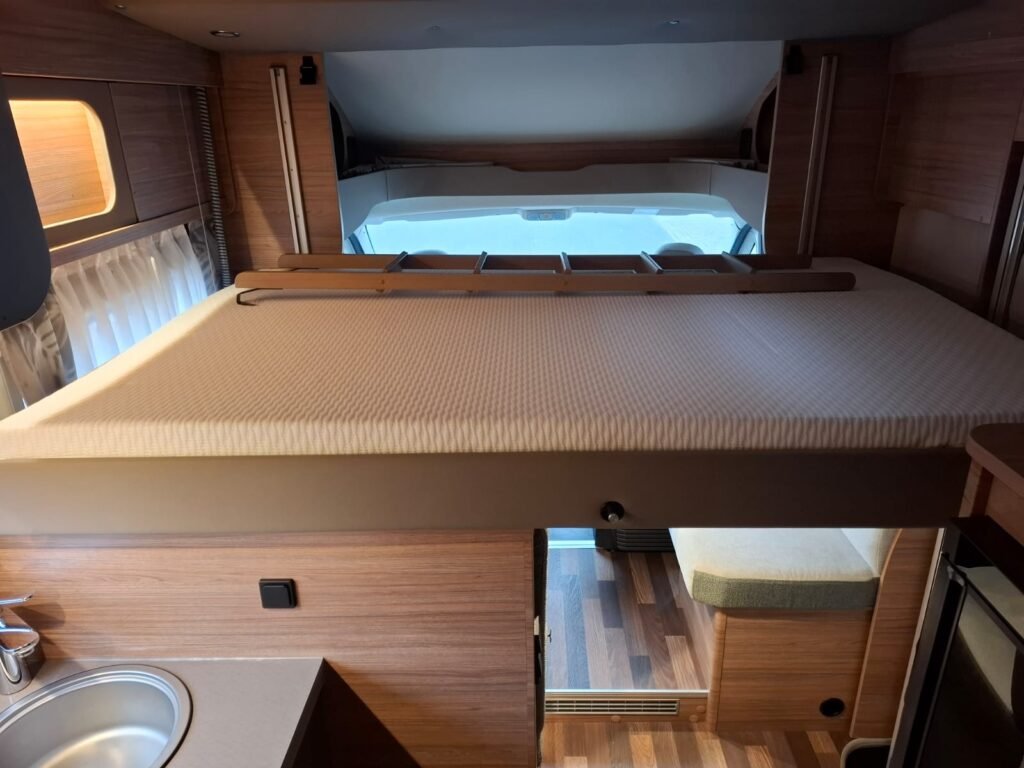 Obrázek interiéru obytného auta s pohodlnou postelí a moderním zázemím. Prostorný a stylový pro komfortní cestování.