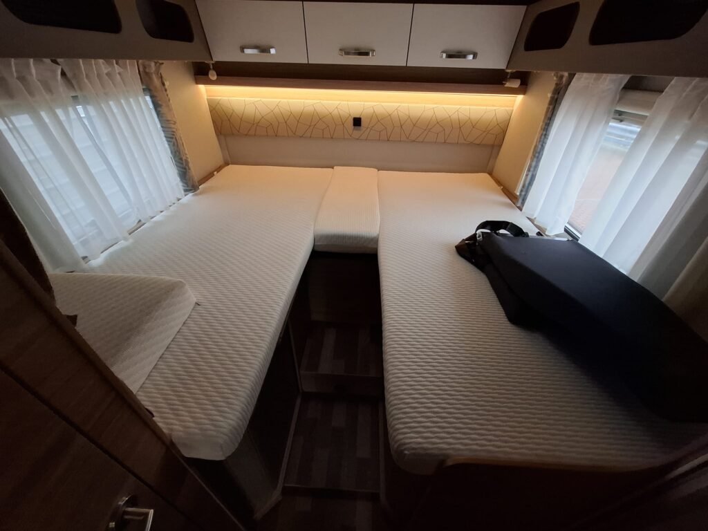 Prostorný interiér obytného auta s dvěma lůžky a moderním osvětlením. Ideální pro pohodlné cestování.