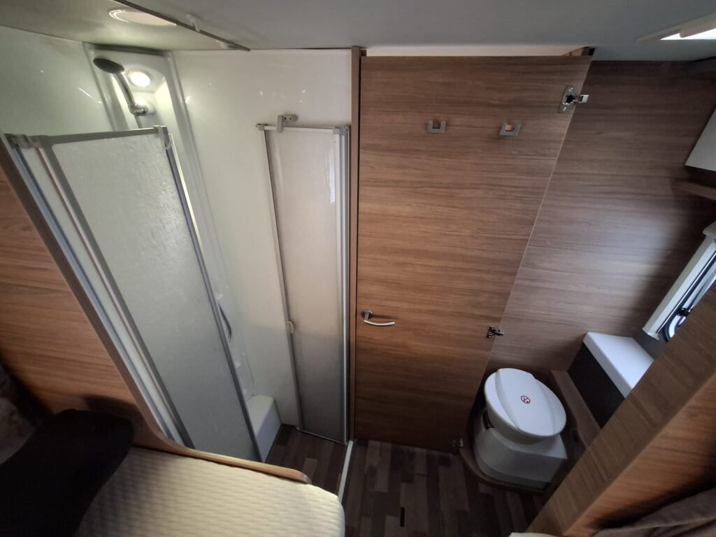 Obrázek interiéru moderního obytného auta s koupelnou a toaletou. Stylové dřevo, prostor pro pohodlí.