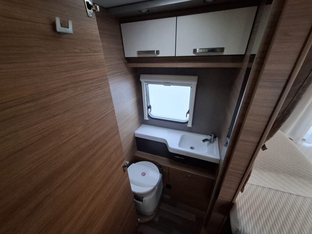 Obrázek interiéru karavanu, zařízeného s umyvadlem a toaletou, s moderním dřevěným dekorem.