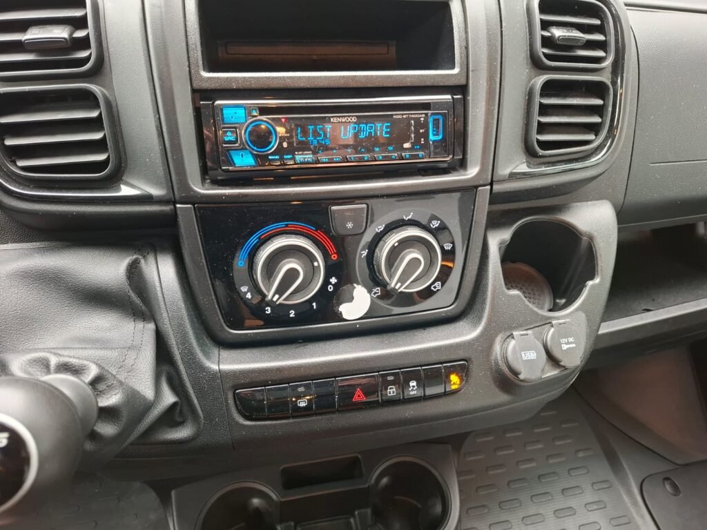 Interiér obytného auta s ovládáním klimatizace a multimediálním systémem. Značka a model nejsou viditelné.