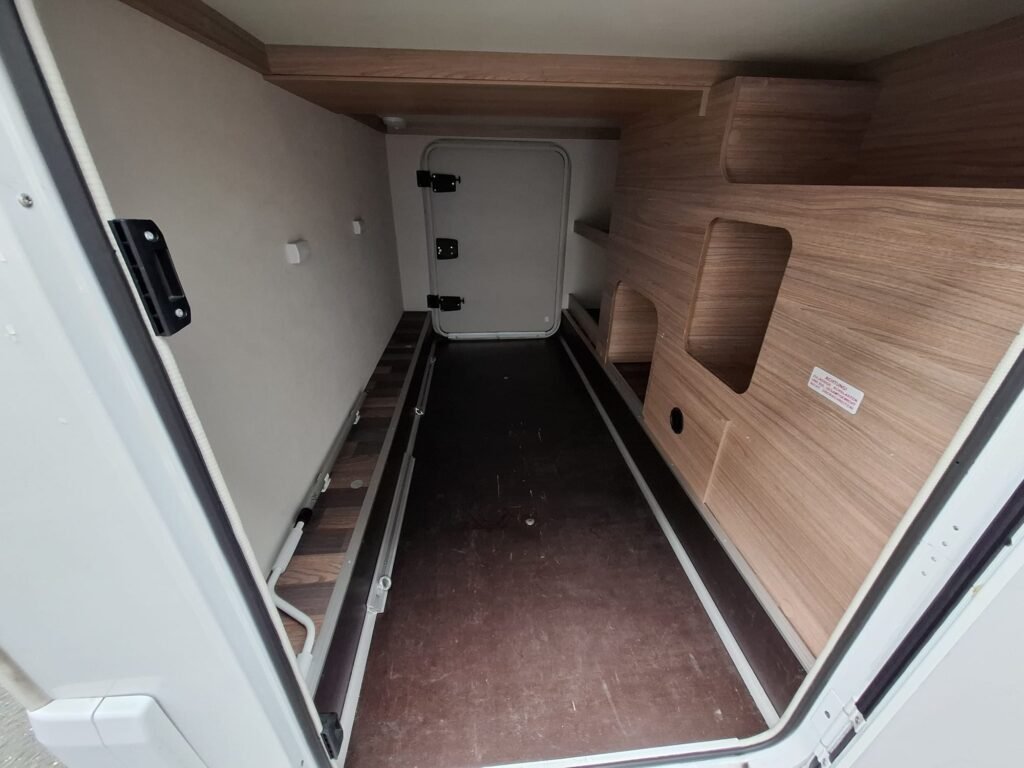 Náhled interiéru obytného auta, prostorný úložný prostor s dřevěnými policemi a pohodlným přístupem.