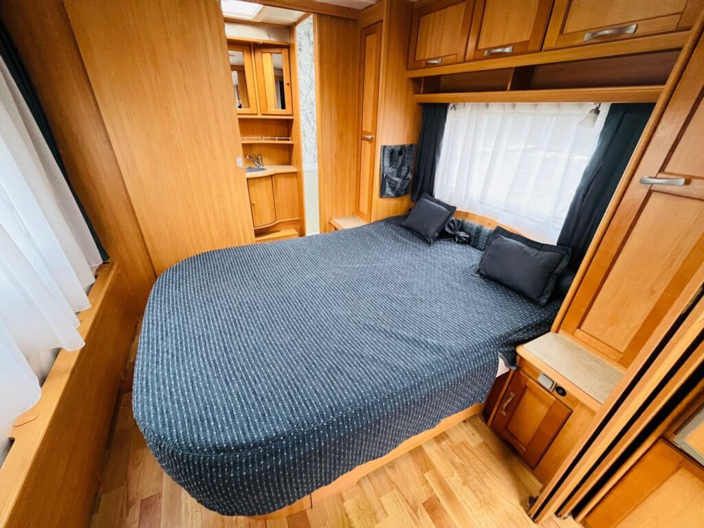 Prostor v karavanu s manželskou postelí a dřevěným nábytkem, ideální na dovolenou.