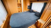 Prostor v karavanu s manželskou postelí a dřevěným nábytkem, ideální na dovolenou.