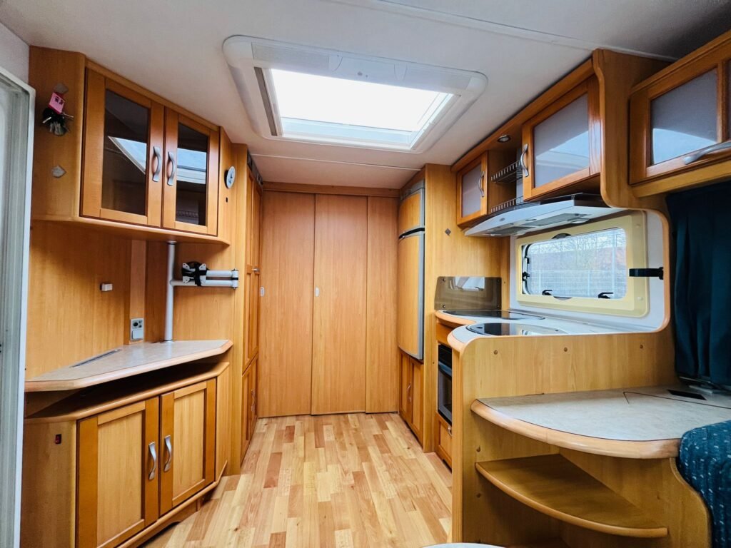 Interiér obytného vozu s dřevěným nábytkem a moderní kuchyní. Ideální pro pohodlné cestování.