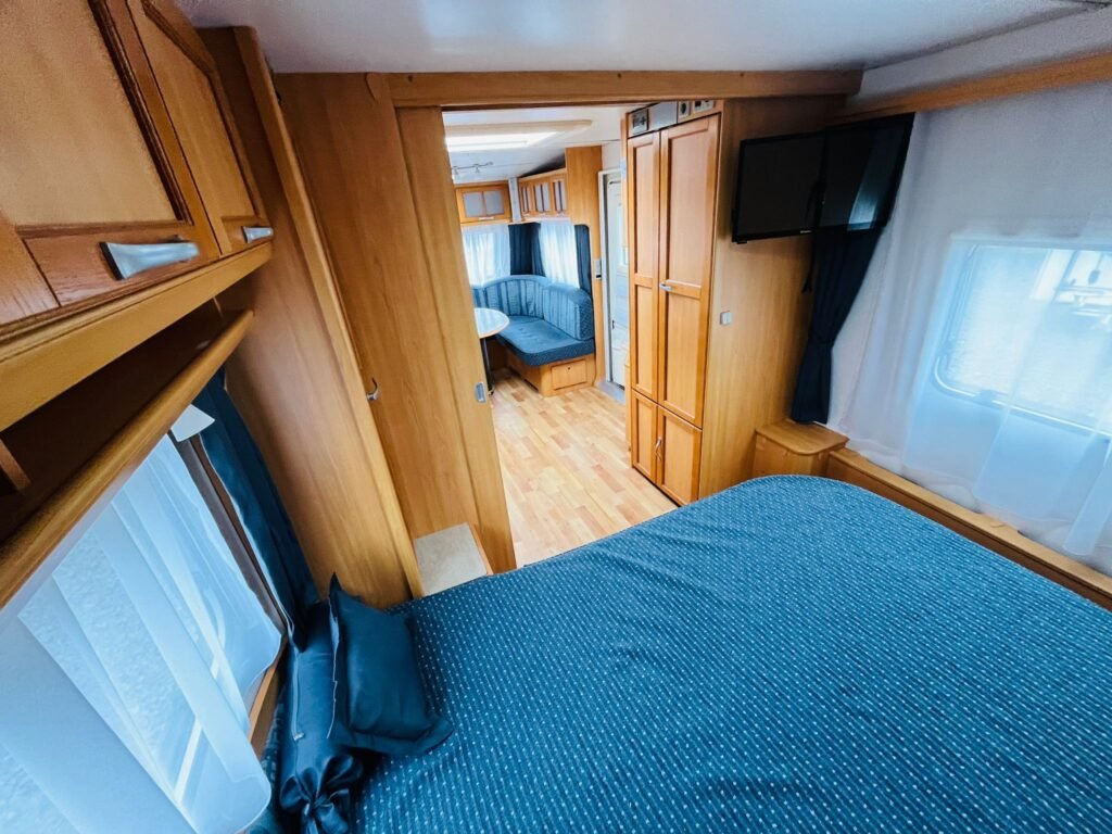 Interiér karavanu s dřevěnými prvky, ložnicí a obývací částí pro pohodlné cestování.