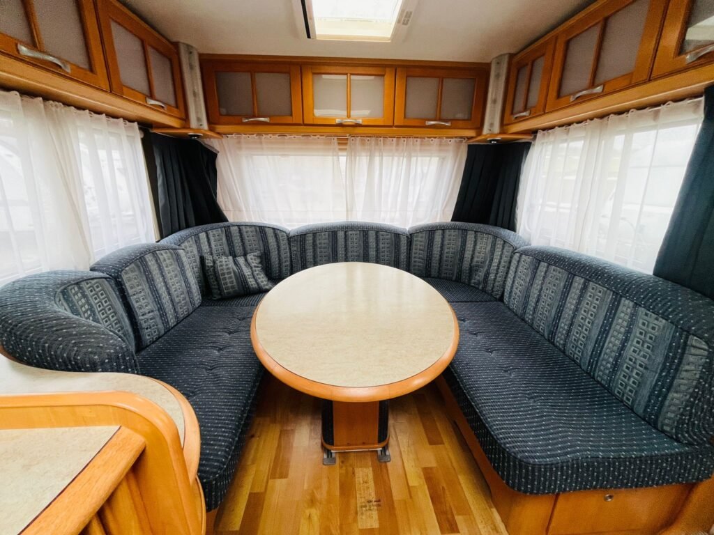 Obrázek interiéru karavanu s pohodlným posezením a velkým stolečkem. Ideální pro rodinné výlety.