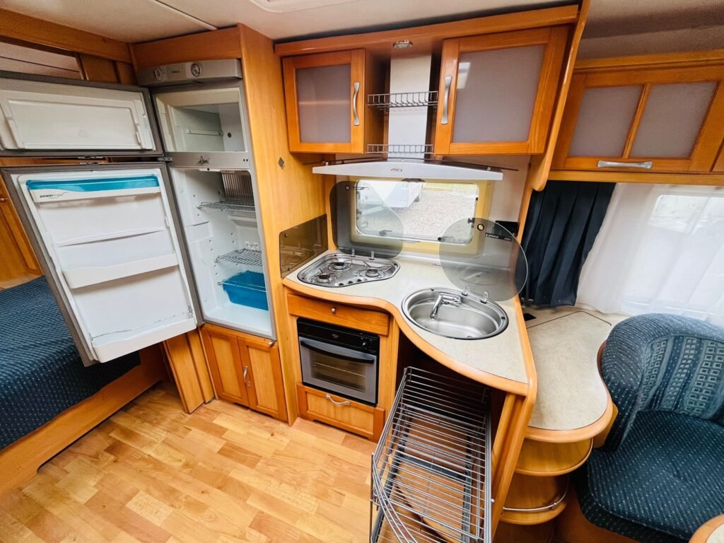 Interiér obytného auta s moderní kuchyní, včetně lednice, sporáku a pohodlného sezení. Ideální pro cestování.