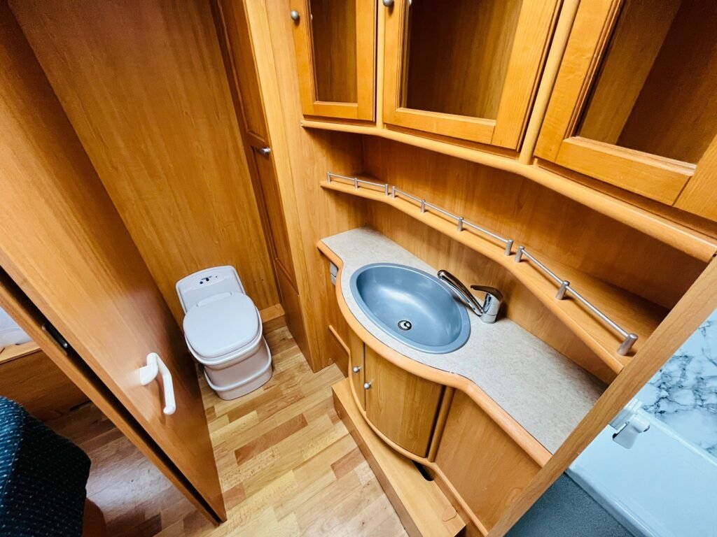 Obrázek interiéru s umyvadlem a toaletou v karavanu. Moderní design a praktické úložné prostory.