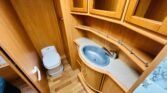 Obrázek interiéru s umyvadlem a toaletou v karavanu. Moderní design a praktické úložné prostory.