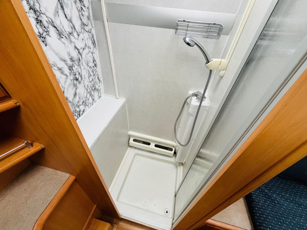 Obrázek zobrazuje sprchový kout v obytném autě, elegantní interiér a praktické uspořádání.