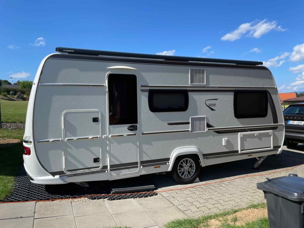 Karavan Saphir zaparkovaný na dobře udržované ploše s modrou oblohou a bílými mraky.