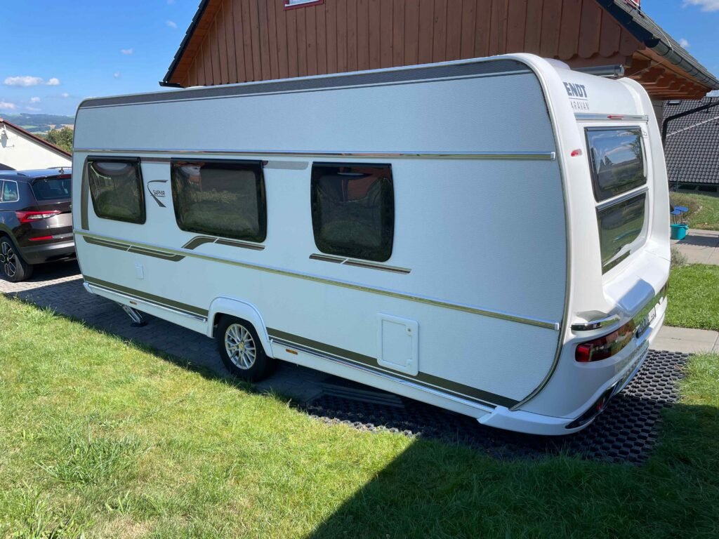 Karavan Enduro Sapphire stojí na trávníku, vedle něj se nachází osobní auto. Ideální pro pohodové cestování.