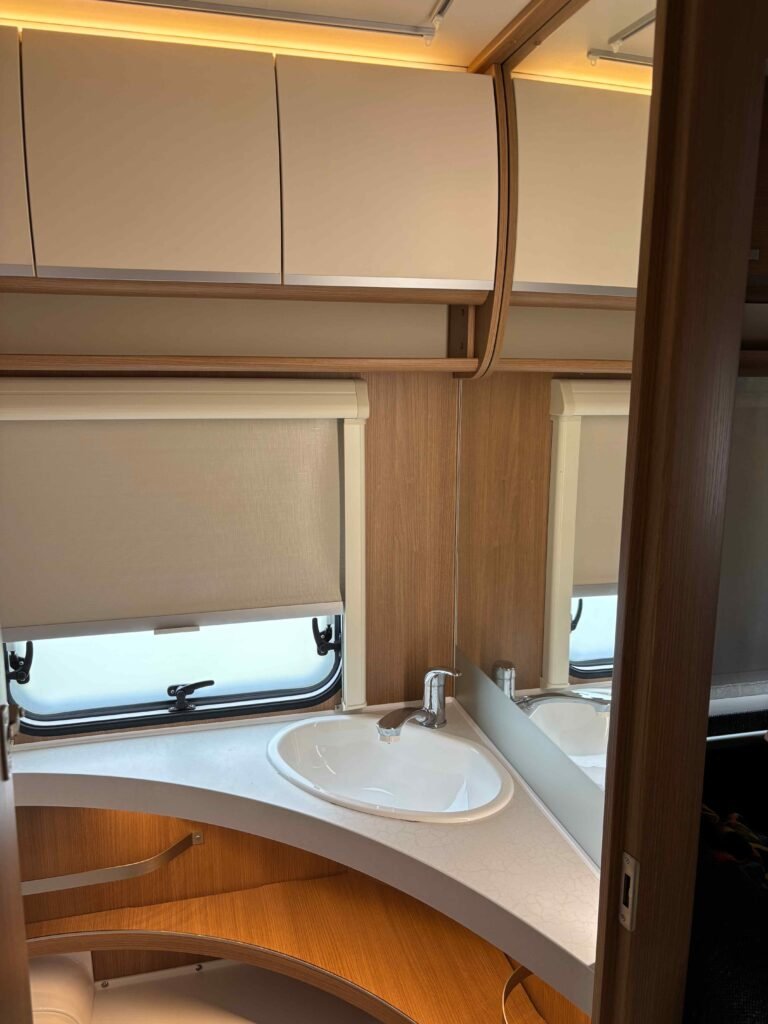Obrázek zachycuje interiér karavanu s umyvadlem a osvětlením. Elegantní design a praktické uspořádání prostoru.