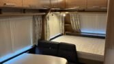 Interiér karavanu s kuchyňským stolem a sedačkami. Viditelná postel a úložné skříně. Moderní a prostorný design.