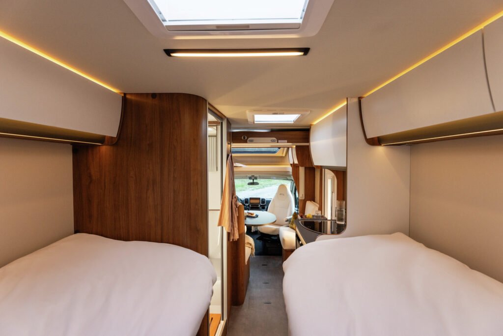 Interiér obytného auta s dvěma lůžky, útulný design a moderní vybavení, ideální pro kempování.