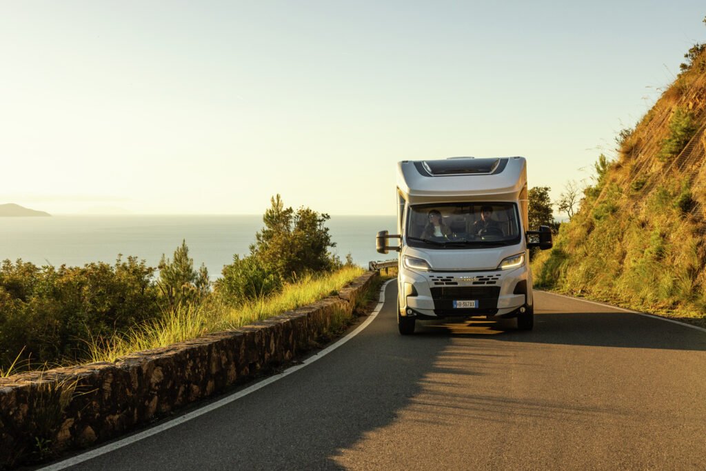 Na silnici se pohybuje obytné auto s elegantním designem v malebné krajině u moře.