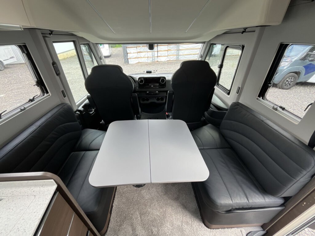 Interiér obytného auta s pohodlnými sedadly a stolem. Značka a model nejsou uvedeny.