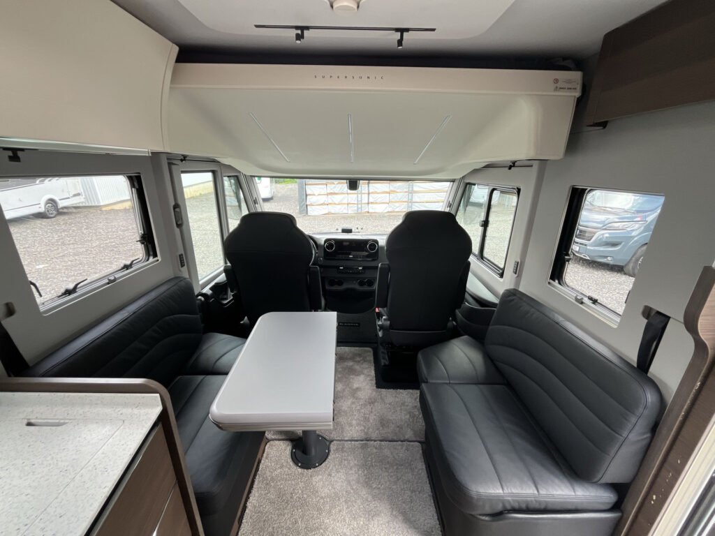 Interiér obytného auta s pohodlnými sedadly a stolem pro čtyři osoby. Značka a model nejsou uvedeny.