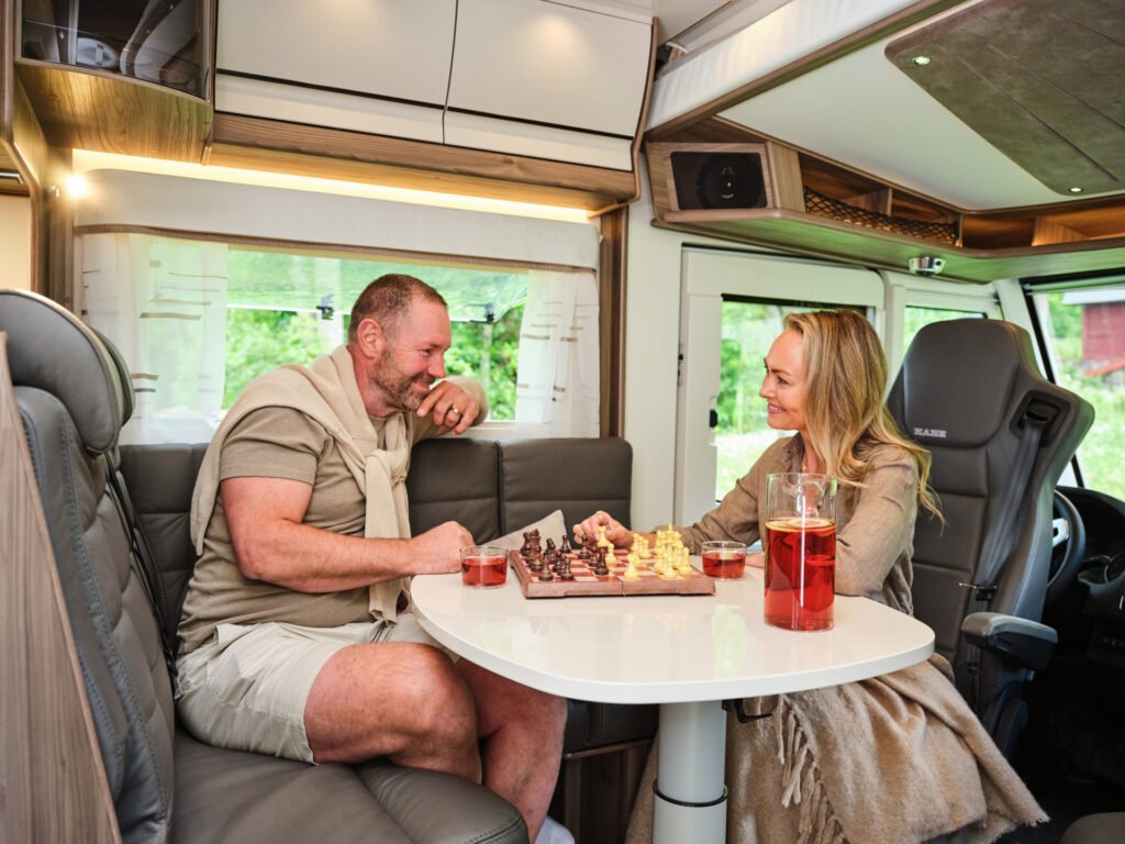Interiér obytného auta se dvěma lidmi hrajícími šachy a osvěžujícími nápoji. Relaxační atmosféra na cestách.