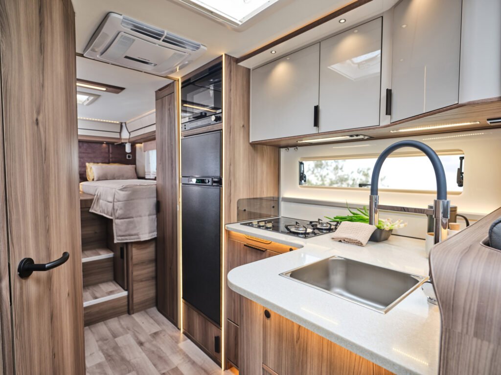 Obrázek interiéru obytného auta s moderní kuchyní a komfortním prostorem na spaní.