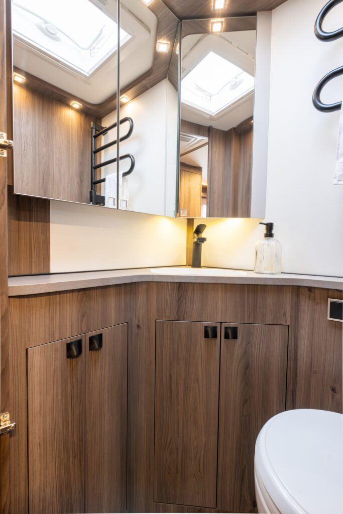 Obrázek interiéru karavanu s moderním designem, dřevěným dekorem a koupelnovými doplňky.
