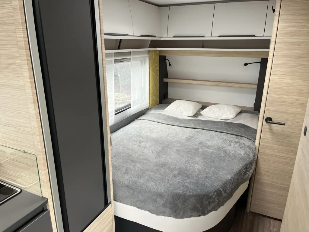 Interiér obytného auta s manželskou postelí a moderním designem. Ideální pro pohodlné cestování.