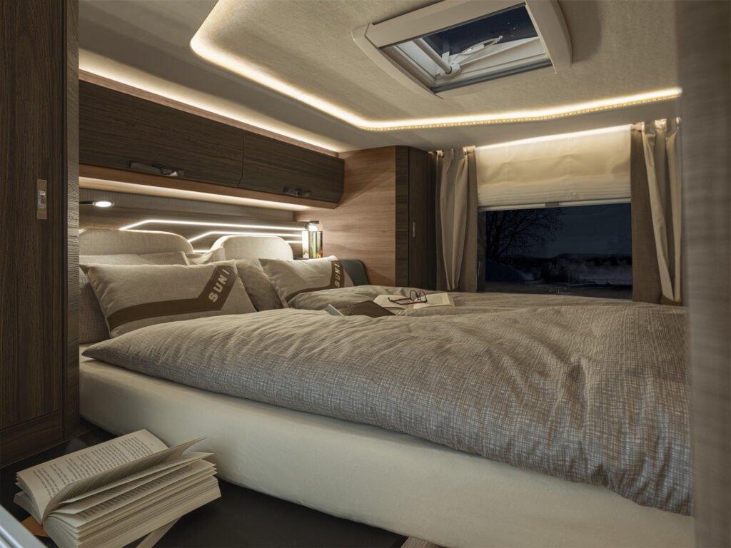 Obrázek ukazuje interiér obytného auta s pohodlnou postelí a moderním osvětlením.