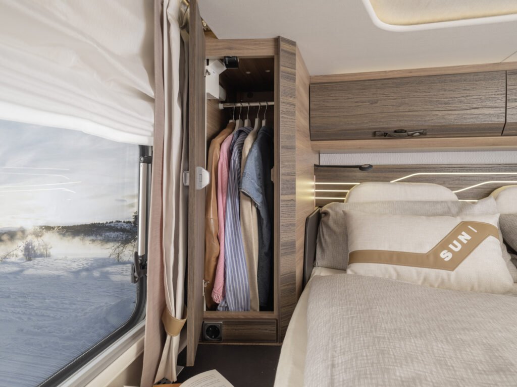 Interiér obytného auta s úložným prostorem a výhledem na zasněženou krajinu.