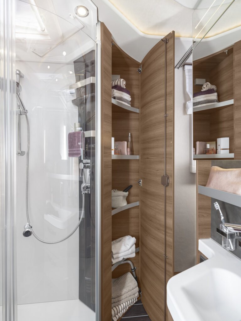 Obrázek interiéru moderního obytného auta s elegantní koupelnou a praktickým úložným prostorem.