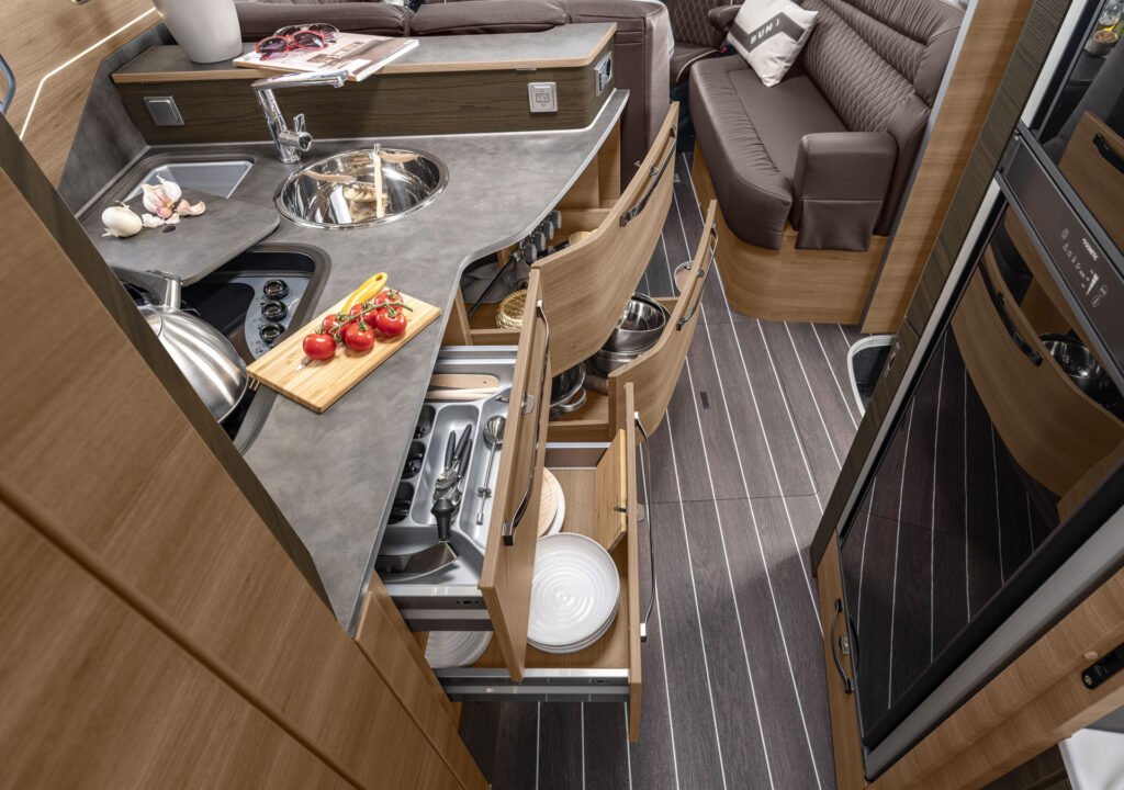 Obrázek kuchyně v obytném voze s moderním designem. Dostatek úložného prostoru a funkční vybavení.