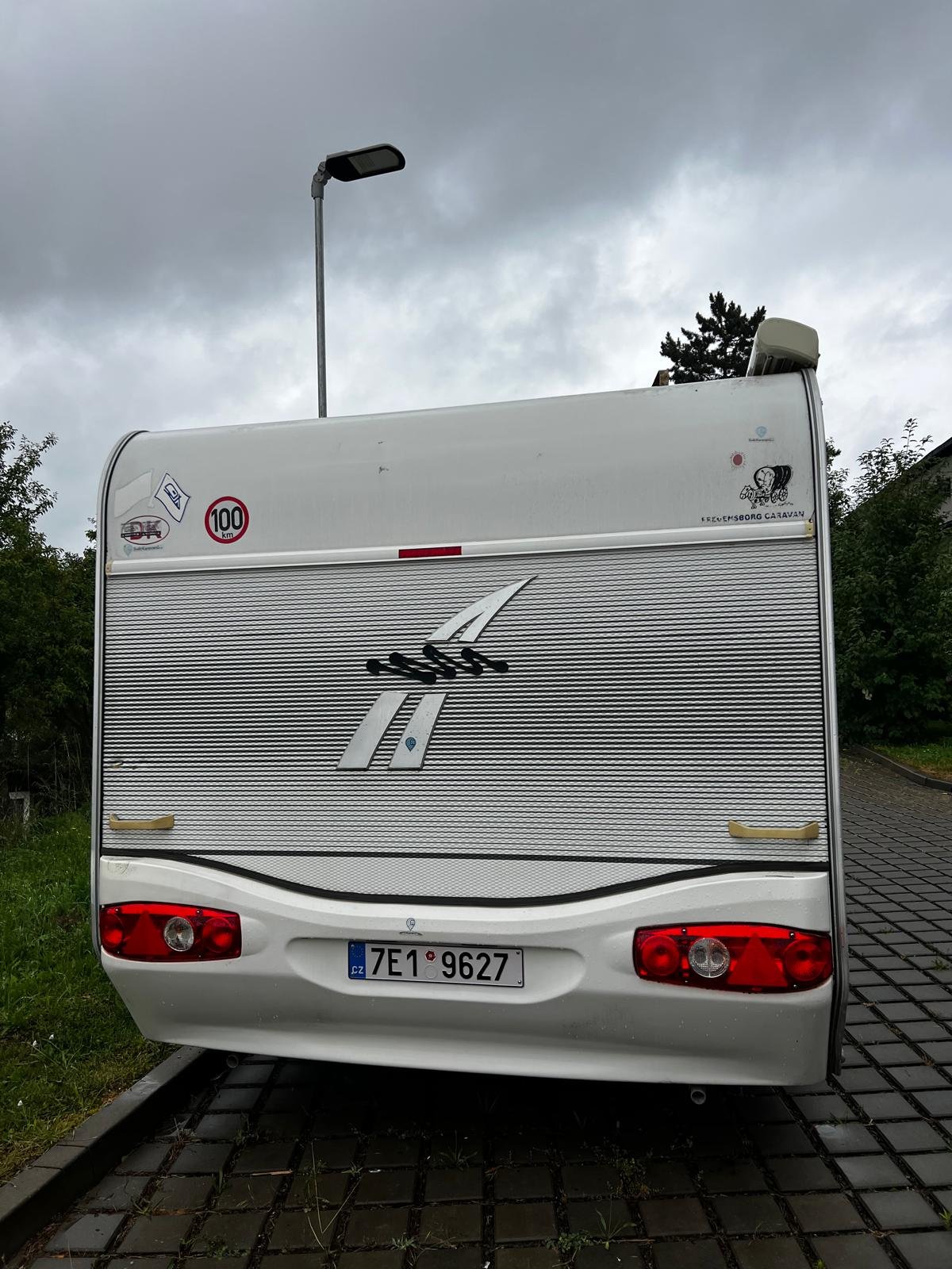 Karavan značky neznámá, typ neviditelný, na pozadí šedá obloha, parkovaný na kamenitém povrchu.