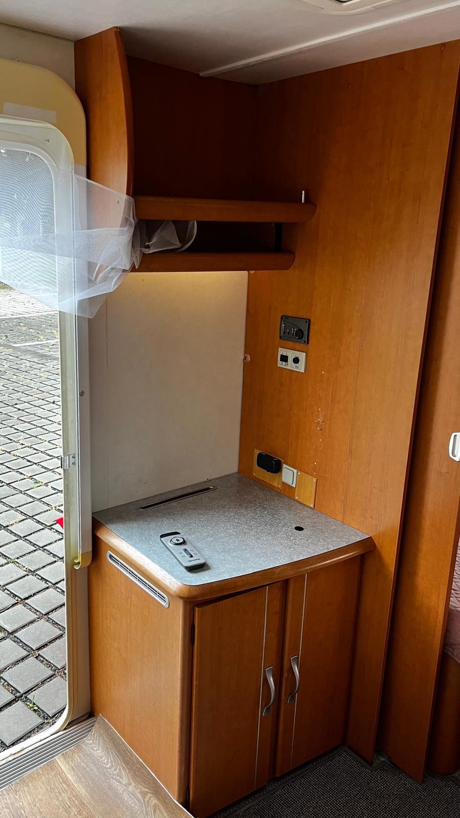 Interiér karavanu s kuchyňskou linkou a úložným prostorem. Elegantní dřevo a praktická dispozice.