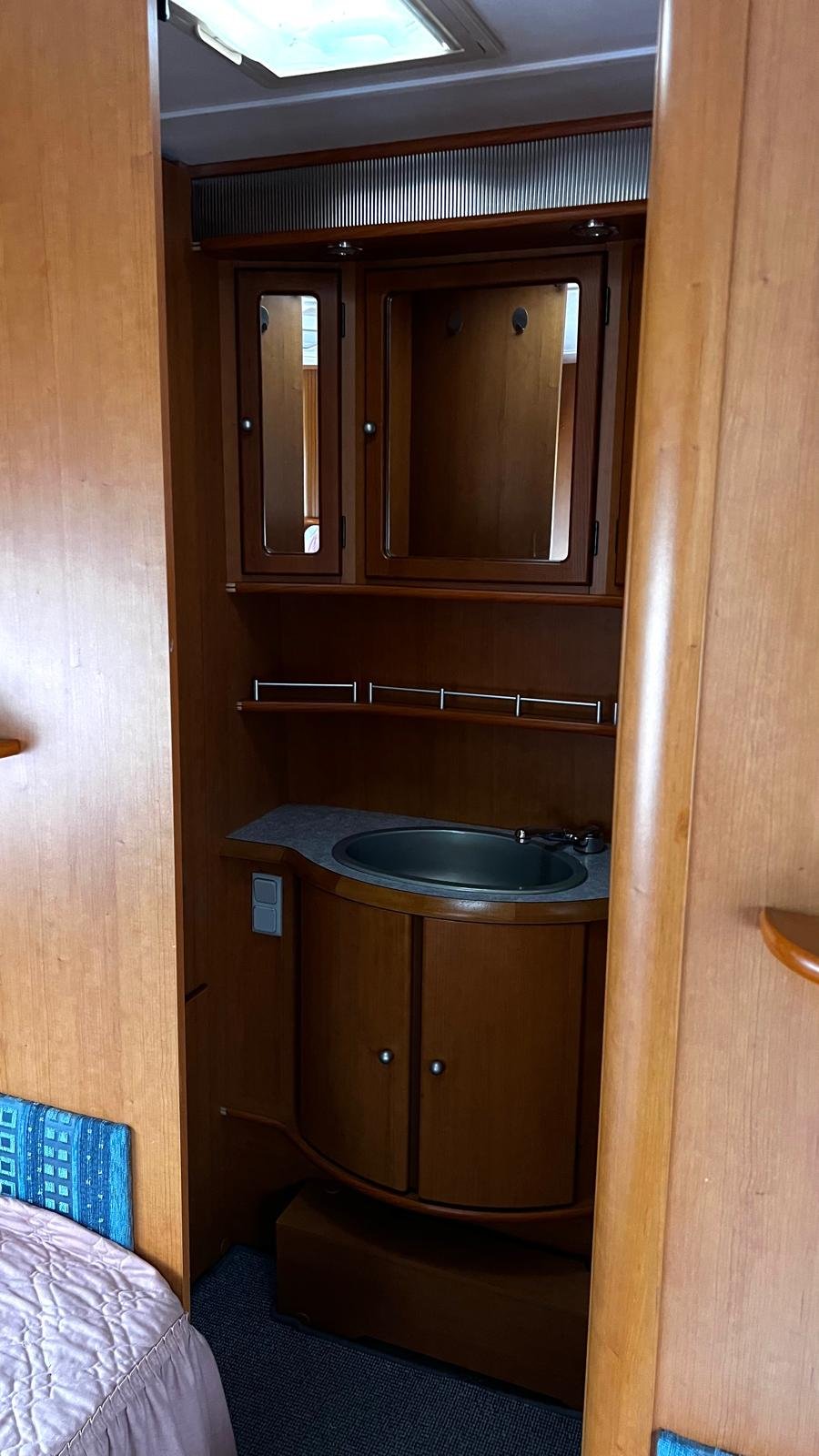 Obrázek interiéru karavanu s dřevěnými prvky a umyvadlem, ideální pro pohodlné cestování.