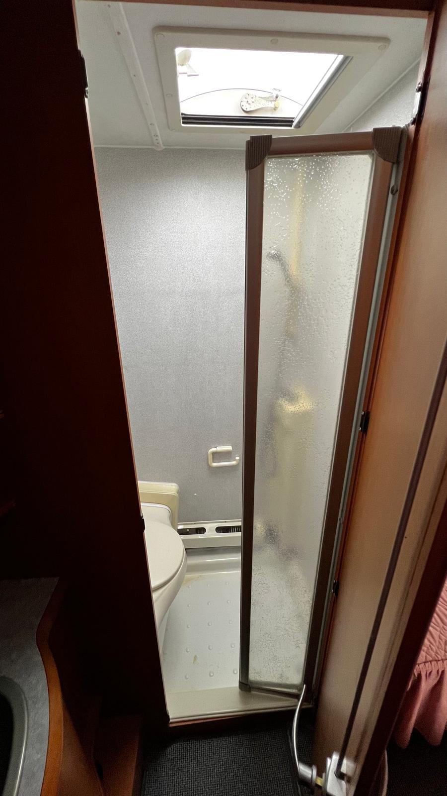 Obrázek interiéru obytného vozu s koupelnou, sprchou a toaletou. Moderní a praktické uspořádání pro cestování.