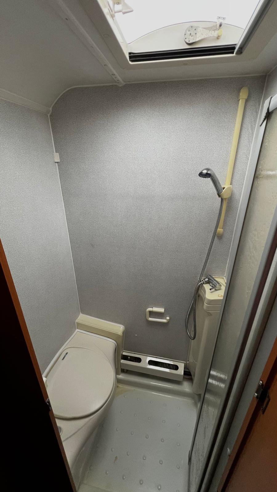 Koupelna karavanu, zahrnující toaletu a sprchu. Ergonomický design pro komfortní využití na cestách.