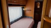 Interiér karavanu s dvěma lůžky a útulným designem, ideální pro pohodlné cestování.