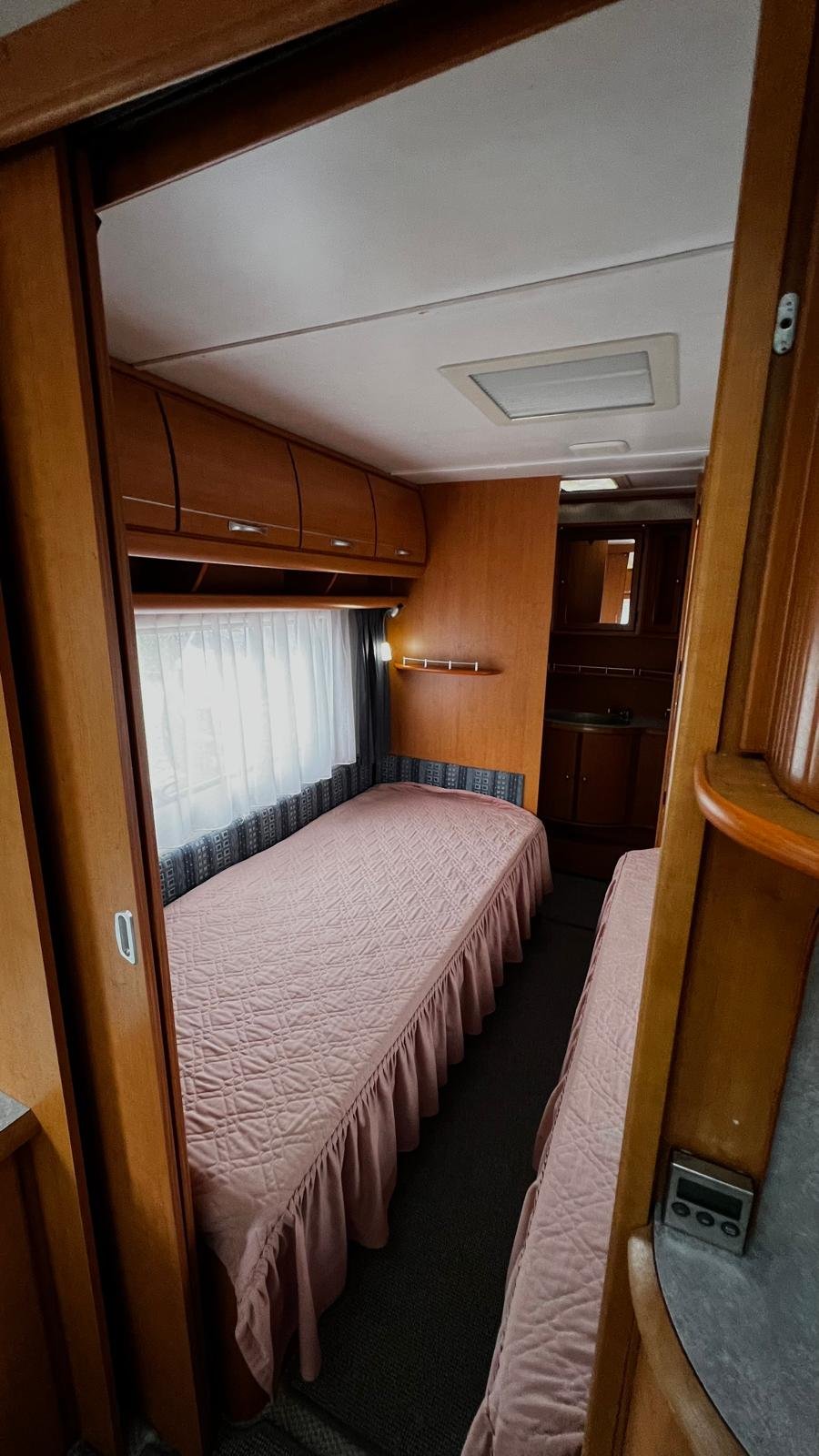Interiér karavanu s dvěma lůžky a útulným designem, ideální pro pohodlné cestování.